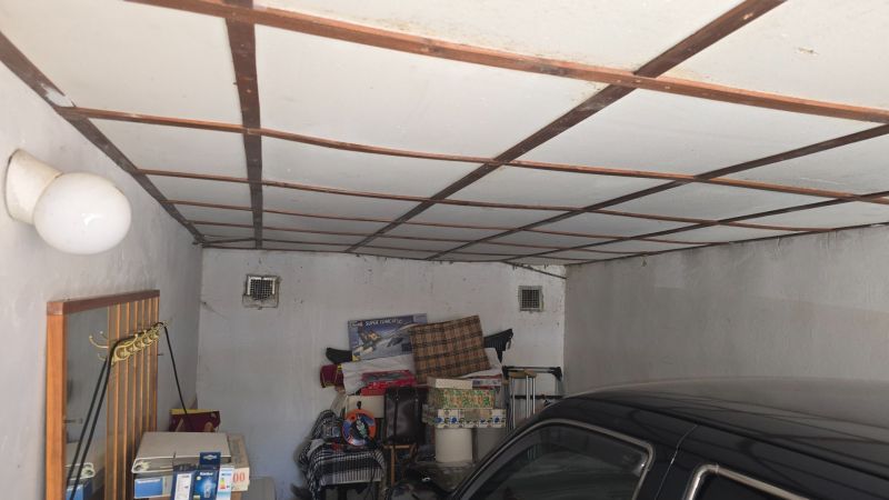 Garáže s bílým ventilátorem, uskladněnými věcmi a zaparkovaným autem.