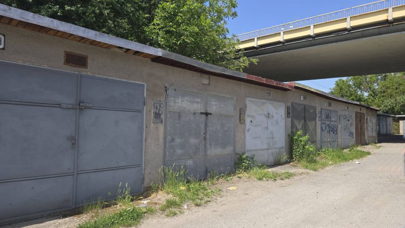 Garáže na Jesenského ulici ve Zvolenu podél cesty se zelení a graffiti.