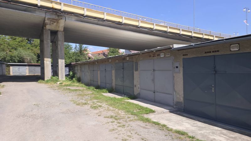 Garáže na Jesenského ulici ve Zvolenu pod mostem, obklopené zelení a štěrkovou cestou.