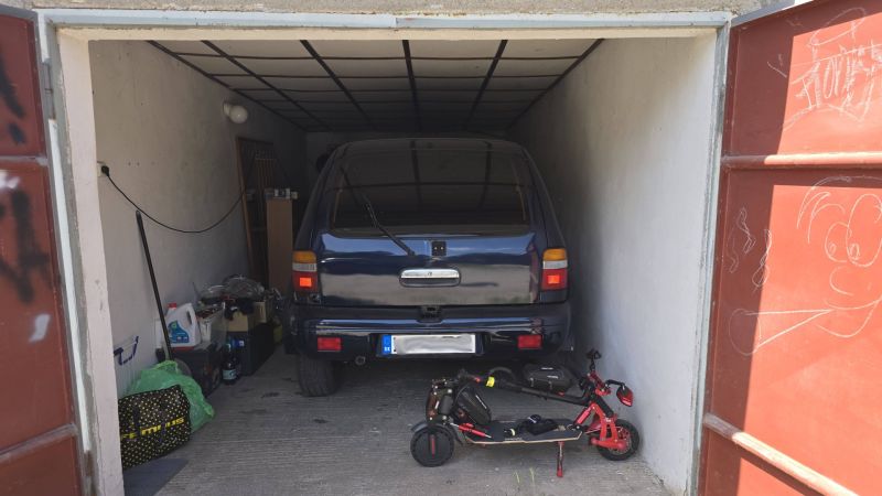 Garáž s autem a elektrickou koloběžkou, uloženými předměty a kresbou na dveřích.