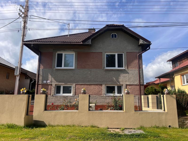 Rodinný dům v Bacúchu obklopený zahradou a oplocením pod modrou oblohou.