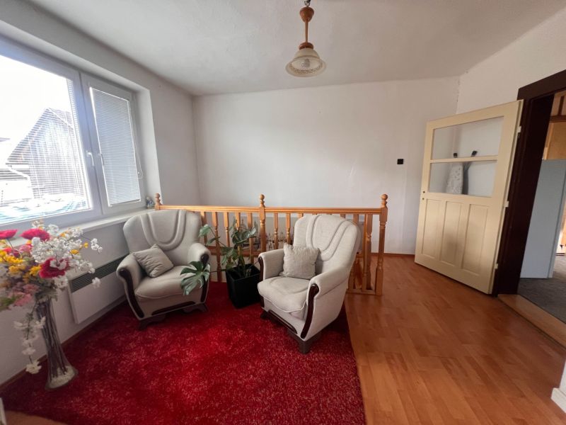 Interiér rodinného domu s pohovkami, červeným kobercem a podlahou s dřevěným dekorem.