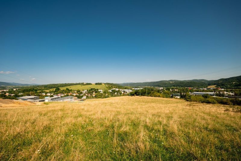 Krajina s travnatou loukou a vesnicí v pozadí v okrese Banská Bystrica, Banskobystrický kraj, vhodná pro Pozemky - bydlení.