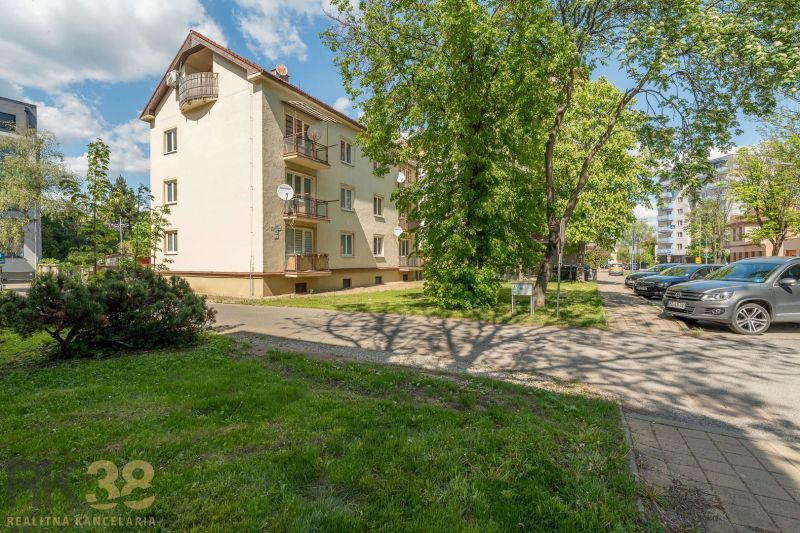 Exteriér budovy s 3-pokojovým bytem v Popradu, obklopený zelení a parkovištěm.