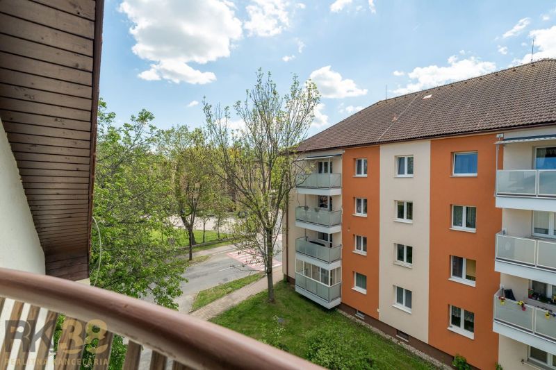 Výhled z balkonu 3pokojového bytu v Popradu na okolní zeleň a bytovou budovu.