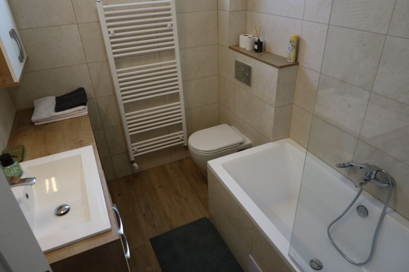 Koupelna v 2-pokojovém bytě s vanou, umyvadlem a podlahou s dřevěným dekorem.