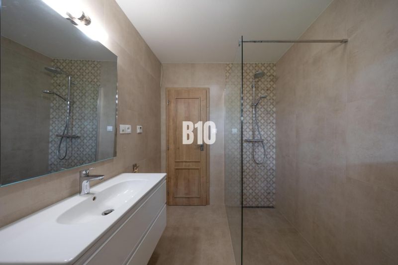 Moderní koupelna s velkým zrcadlem, sprchovým koutem a minimalistickým vybavením.