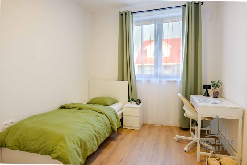 Jednoduchý pokoj se zeleným povlečením a podlahou s dřevěným dekorem.