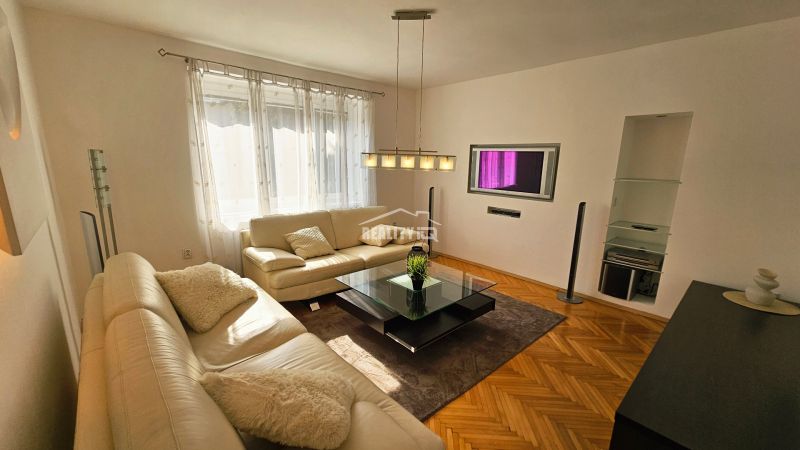 Obývací pokoj s bílou sedačkou a podlahou s dřevěným dekorem ve 2pokojovém bytě.