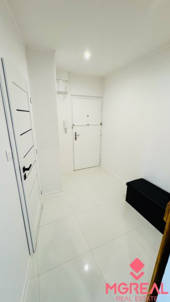 Bílá vstupní chodba s dlažbou a tmavou lavicí v 1-pokojovém bytě.