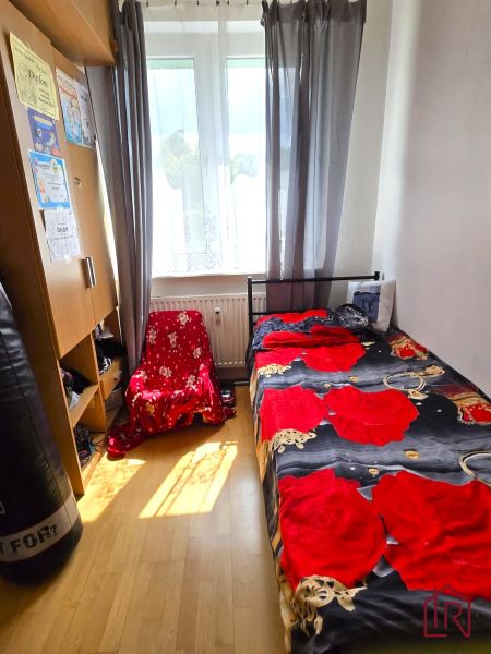 Pokoj ve 4pokojovém bytě s postelí, skříní a podlahou s dřevěným dekorem.