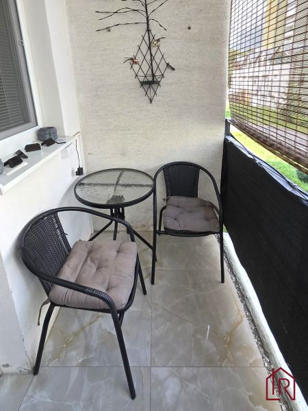Balkon ve 4pokojovém bytě se dvěma židlemi a stolkem na dlažbě.