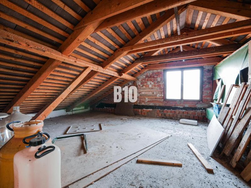 Podkroví rodinného domu s dřevěným trámovým stropem a cihlami.