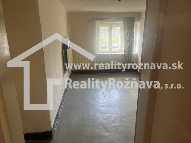 Pokoj v rodinném domě s betonovou podlahou a oknem, kterým přichází světlo.
