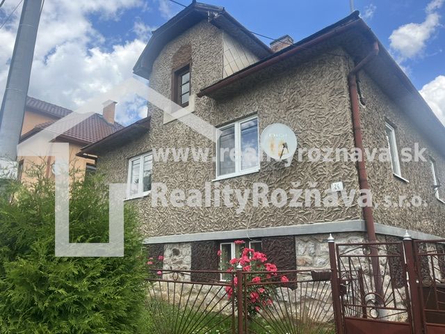 Rodinný dům v Rudné s texturovanou fasádou, zeleným plotem a květinami v zahradě.