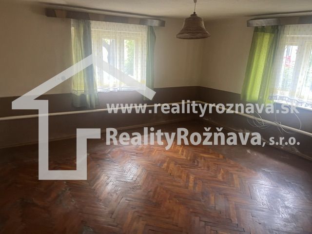 Interiér rodinného domu s podlahou s dřevěným dekorem a zelenými závěsy.