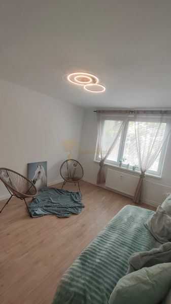 Pokoj ve 4pokojovém bytě s podlahou s dřevěným dekorem, křesly a osvětlením.