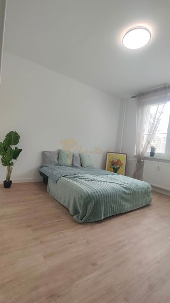 Světlý pokoj s postelí, pokojovou rostlinou a podlahou s dřevěným dekorem ve 4-pokojovém bytě.