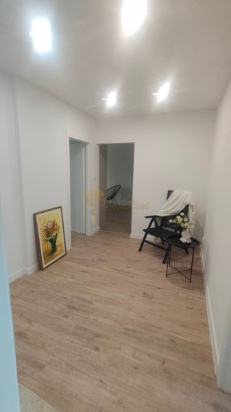 Interiér 4-pokojového bytu s podlahou s dřevěným dekorem, křeslem a obrazem.