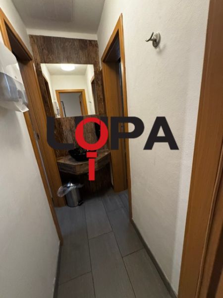 Chodba obchodních prostor s tmavou podlahou a bílými stěnami.