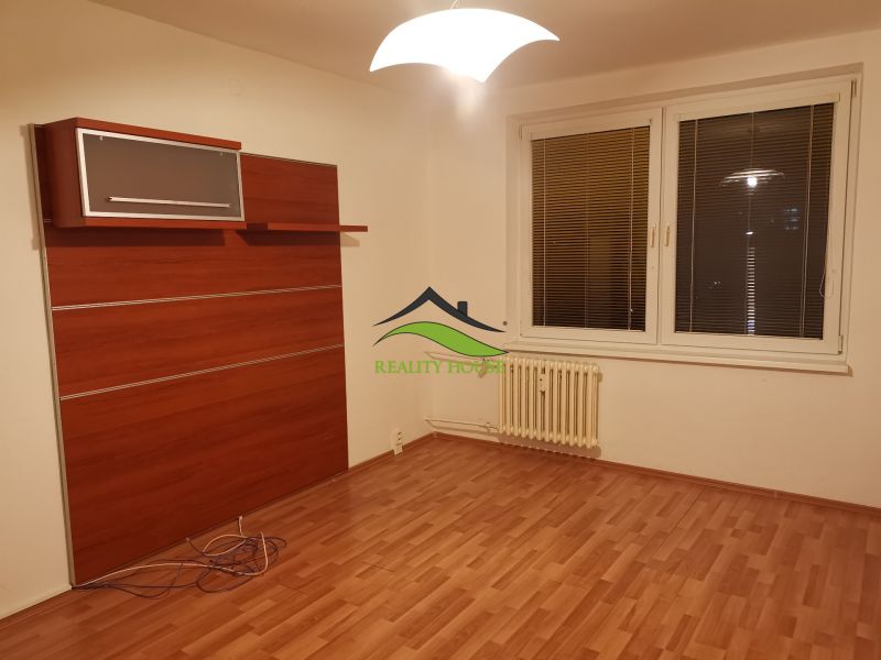 Pokoj s podlahou s dřevěným dekorem, bílými stěnami a nástěnnou skříní ve 3-pokojovém bytě.