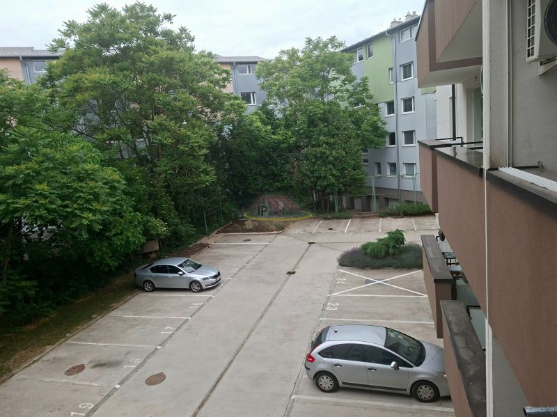Parkoviště na Sportovní ulici v Dunajské Lužné s auty a zelení v pozadí.