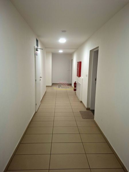 Chodba s bílými stěnami, dlažbou a nouzovým vybavením v garsonce.