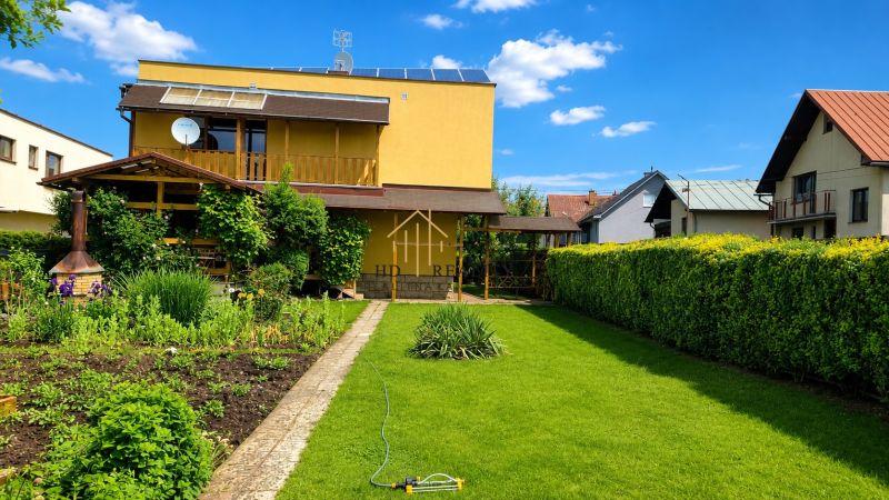 Zahrada a rodinný dům ve Slovenské Ľupči s upraveným trávníkem a květinovými záhony.