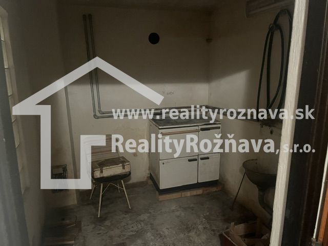 Malá místnost s kuchyňským sporákem, umyvadlem a betonovou podlahou, vhodná pro chatu.