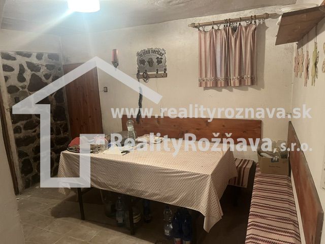 Jídelní kout s ubrusem, lavicí a kamenem na stěně v chatě.