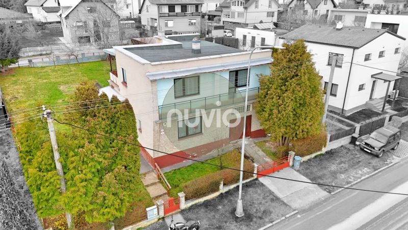 Dvoupatrový rodinný dům v Martině se zahradou, obklopený stromy a oplocením.