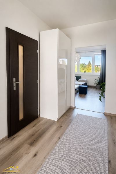 Chodba v 2-pokojovém bytě s podlahou s dřevěným dekorem, vedoucí do obývacího pokoje.