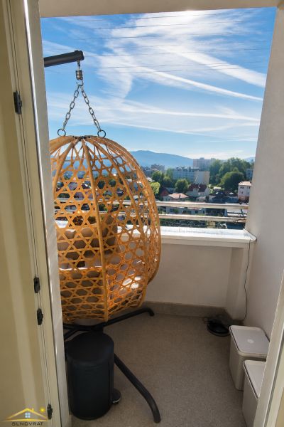 Balkon v 2-pokojovém bytě s ratanovým křeslem a výhledem na město.