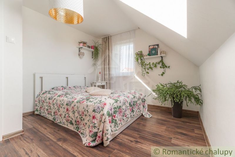 Světlá ložnice v rodinném domě s podlahou s dřevěným dekorem a rostlinami.