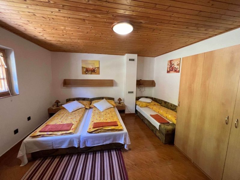 Ložnice s dřevěným stropem, třemi postelemi a podlahou s dřevěným dekorem v rodinném domě.