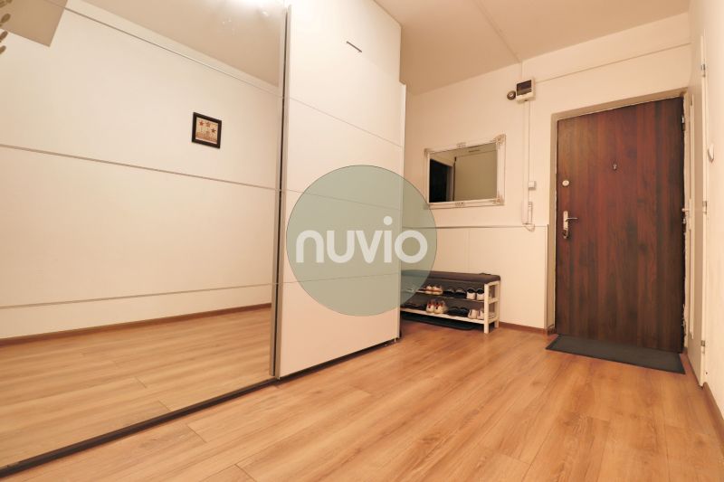 Předsíň s podlahou s dřevěným dekorem v 2-pokojovém bytě s velkým zrcadlem a botníkem.