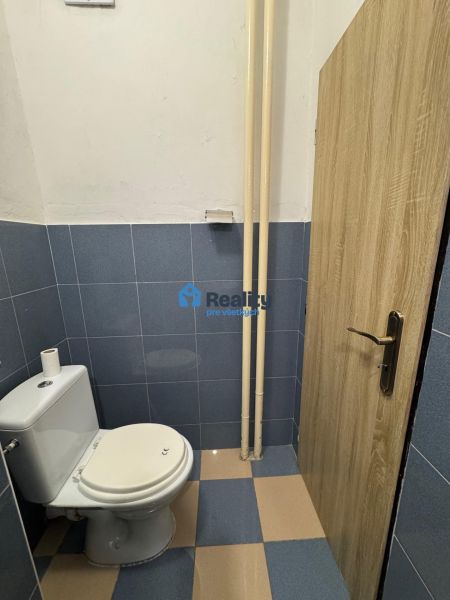Toaleta s modrými dlaždicemi v dvoupokojovém bytě, dveře s dřevěným dekorem.