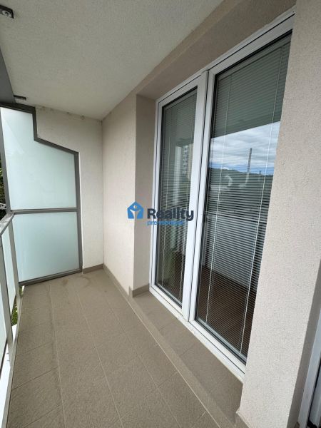 Balkon 2-pokojového bytu s dlaždicovou podlahou, zábradlím a prosklenými dveřmi.