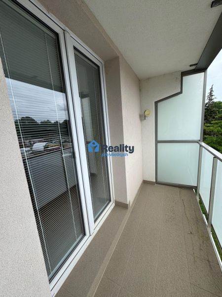 Balkon v 2-pokojovém bytě se skleněným zábradlím a dlaždicovou podlahou.