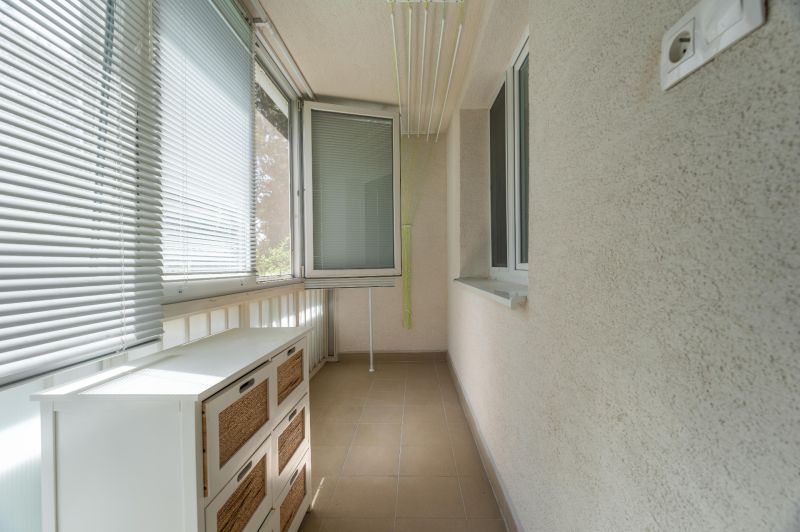 Zasklená lodžie s bílými žaluziemi a skříní v 3-pokojovém bytě.