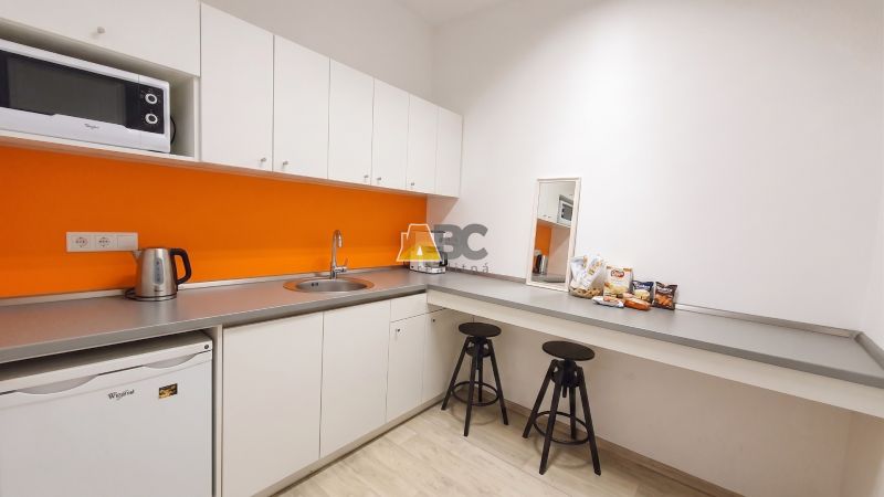 Kanceláře s kuchyňkou, bílými skříňkami, oranžovou stěnou a podlahou s dřevěným dekorem.