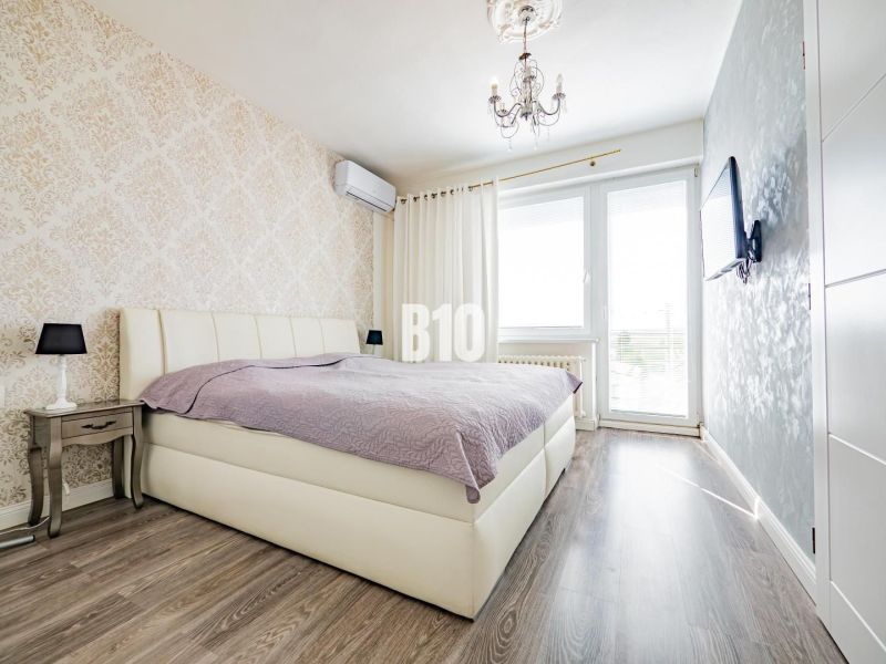 Ložnice s postelí, vzorovanou tapetou a podlahou s dřevěným dekorem v rodinném domě.