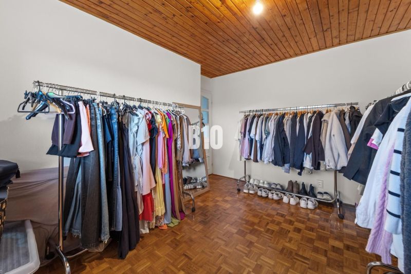 Šatna v rodinném domě s věšákovými tyčemi a podlahou s dřevěným dekorem.