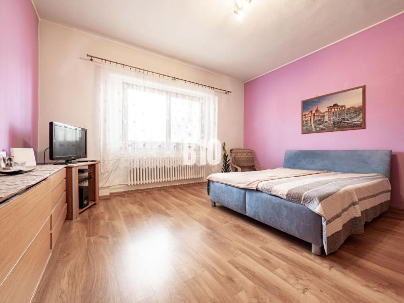 Ložnice v rodinném domě s podlahou s dřevěným dekorem, nábytkem a televizí.