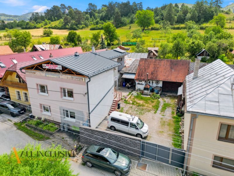 Rodinný dům v Dúbravici obklopený zelení s parkováním a sousedními budovami.
