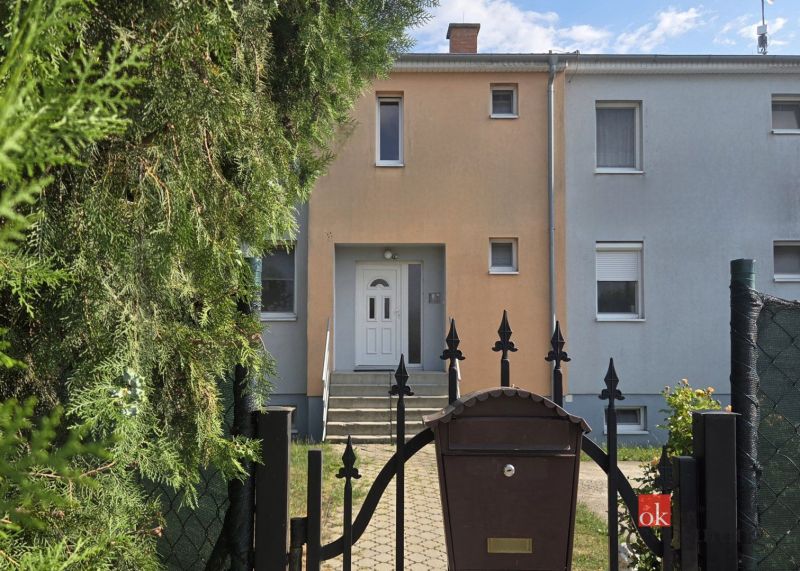 Vstup do řadového domu s brankou, dřevinami a poštovní schránkou v Blatné na Ostrově.