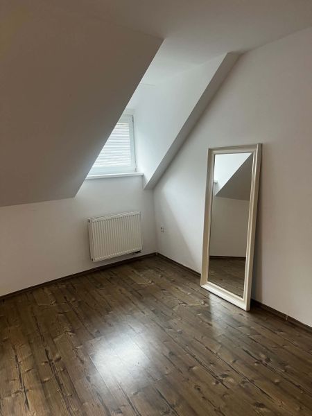 Podkrovní pokoj s podlahou s dřevěným dekorem a velkým zrcadlem v 2pokojovém bytě.