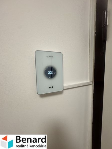 Termostat na stěně v 2-pokojovém bytě, teplota nastavena na 22 °C.