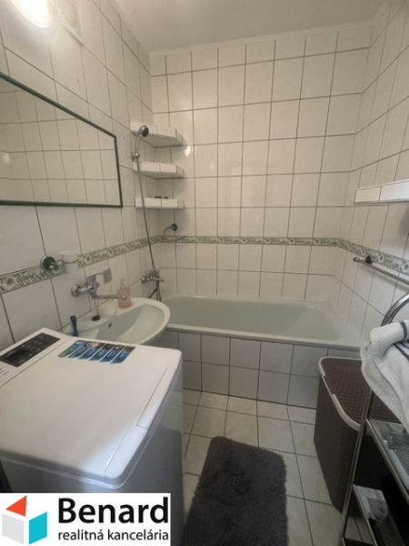 Koupelna v 2-pokojovém bytě s vanou, umyvadlem a pračkou, obložená bílými dlaždicemi.