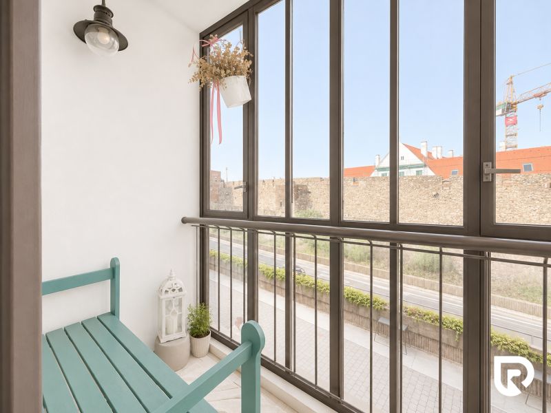 Zasklený balkon 2pokojového bytu s lavičkou, rostlinou a výhledem na městskou ulici.